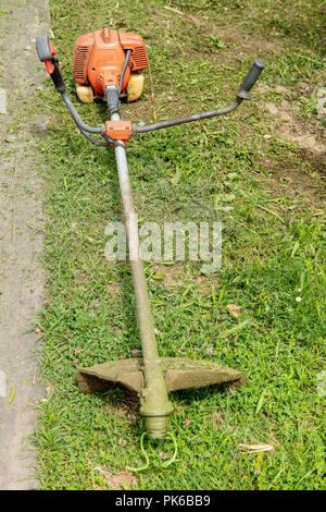 Close up d'une vieille et sale débroussailleuse sur l'herbe verte dans le jardin. Banque D'Images