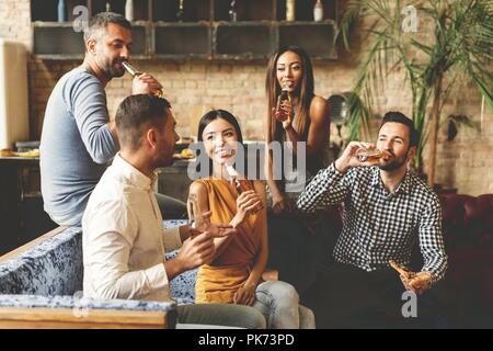 Passer du bon temps avec ses meilleurs amis. Groupe des jeunes gaies jouissant de la nourriture et des boissons tout en dépensant temps agréable dans cofortable des chaises sur la cuisine ensemble. Banque D'Images