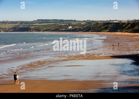 Royaume-uni, Angleterre, dans le Yorkshire, Filey, les visiteurs de marcher sur des sables bitumineux Muston plage à marée basse en soleil Banque D'Images