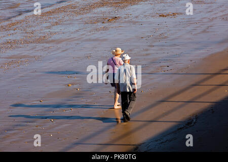 Royaume-uni, Angleterre, dans le Yorkshire, Filey, senior couple en train de marcher sur la plage à marée basse en soleil Banque D'Images