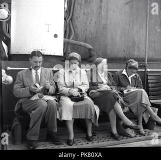 Années 1950, historique, un gentleman britannique fumant une pipe, assis avec trois femmes sur un banc en bois, sur un bateau sur la voile sur le lac Victoria, en Ouganda. Le protectorat britannique d'Ouganda a été un protectorat de l'Empire britannique et de nombreux Britanniques, connu comme les expatriés, a terre et d'élevage. Banque D'Images