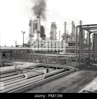 Années 1960, historique, vue extérieure d'une immense raffinerie de pétrole dans le désert, en Arabie Saoudite, montrant une masse de pipelines et à la flamme ou la gravure des tours. Banque D'Images