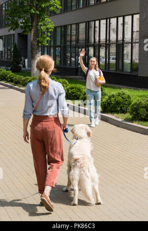 Fille en agitant à la mère pendant qu'elle marche avec chien sur street Banque D'Images