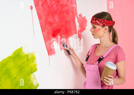 Young woman with coffee cup painting wall en rouge par rouleau à peindre Banque D'Images