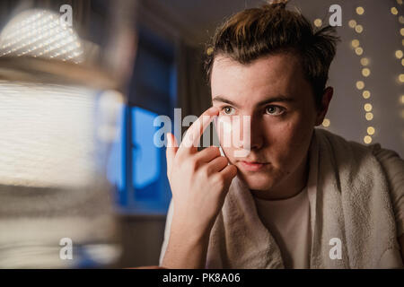 Jeune homme est l'application de la crème pour le visage dans un miroir à la maison. Banque D'Images