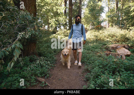 Bel homme promenait son chien dans les bois après un chemin. Heureux golden retriever mâle promenades près de son meilleur ami Banque D'Images