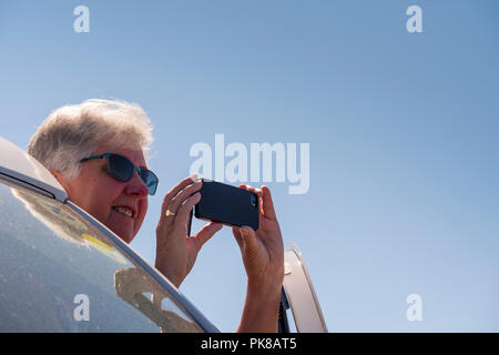 Dame à la porte d'un camping-car à la main pour prendre une photo sur son téléphone portable Banque D'Images