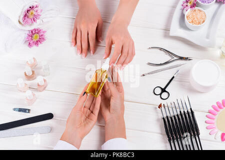 Vue partielle de la femme en tenant la bouteille d'huile d'arome de mains de manucure à table avec ongles, limes à ongles, coupe-ongles, le poussoir de cuticle, mer sal Banque D'Images