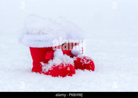 Petit Père Noël feutré rouge bottes avec décoration de la fourrure sur la neige fond de Noël. Banque D'Images