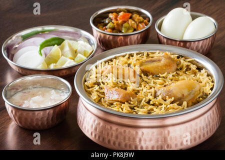 Vue rapprochée de la partie supérieure de délicieux biryani poulet indien servi en salade avec des ustensiles en cuivre authentique (raita), de la sauce et l'oeuf. La lumière naturelle. Banque D'Images