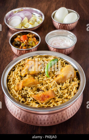 Vue rapprochée de la partie supérieure de délicieux biryani poulet indien servi en salade avec des ustensiles en cuivre authentique (raita), de la sauce et l'oeuf. La lumière naturelle. Banque D'Images