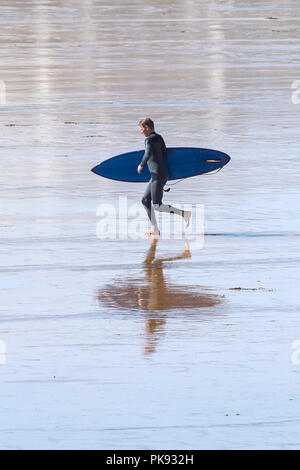 Un surfer carrying his surfboard et courir sur la plage de Fistral Newquay en Cornouailles.