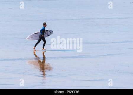 Un surfer carrying his surfboard et courir sur la plage de Fistral Newquay en Cornouailles.