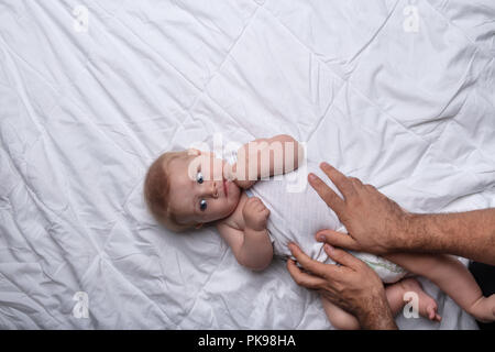 Père de la manipulation en douceur son fils sur un lit dans un geste affectueux posant ses mains sur le bébé car il s'appuie sur le dos vu de passage Banque D'Images