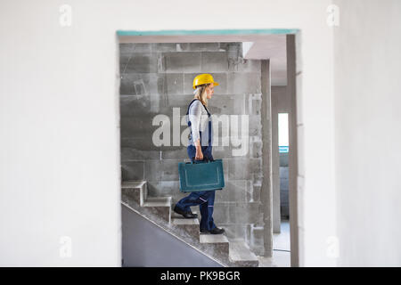 Femme avec une boîte à outils en descendant l'escalier sur le chantier de construction. Banque D'Images