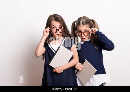 Deux petites écolières surpris avec des lunettes et bouche ouverte debout dans un studio. Banque D'Images