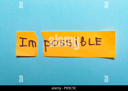 Le mot impossible est écrit sur du papier jaune et déchiré sur fond bleu.le succès et la motivation, concept défi,objectif, réalisation Banque D'Images