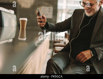 Senior business man wearing earphones écouter chanson de son smart phone at cafe. Smiling businessman in cafe écoutez de la musique avec téléphone. Banque D'Images