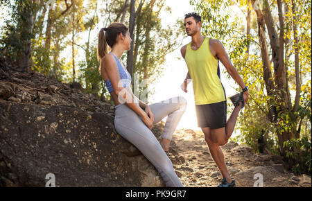 Fit young woman in sportswear assis sur le rocher et se détendre après trail run, avec l'homme qui s'étend de la jambe. L'homme et la femme trail runner prenant br Banque D'Images