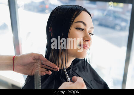 Belle jeune femme ayant fait couper les cheveux chez le coiffeur. Appréciant les processus de création d'un nouveau modèle de cheveux. Banque D'Images