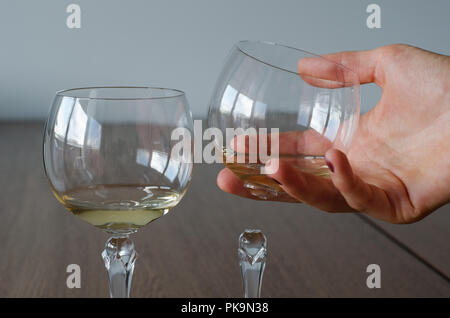 Deux verres à vin. Un verre à moitié plein et un autre à moitié plein verre de vin endommagées dans la main de femme sur fond de table en bois Banque D'Images