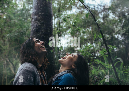 Up avec bouche ouverte un jour de pluie. Heureux l'homme et la femme attraper les gouttes de pluie sur le timon en forêt tropicale. Banque D'Images