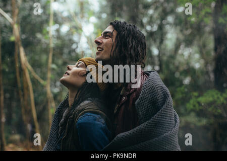 Portrait of young couple couvrant avec mise en veille alors qu'il se tenait sous la pluie en parc. Beau couple de passer du temps ensemble dans la pluie. Banque D'Images