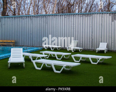 Près de la piscine avec eau chaude thermale il y a des chaises longues en plastique blanc sur un terrain artificiel vert à Paratunka au Kamtchatka Banque D'Images