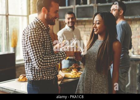 Partie avec ses meilleurs amis. Group of cheerful young people enjoying home party avec des collations et des boissons tout en communiquant sur la cuisine. Banque D'Images