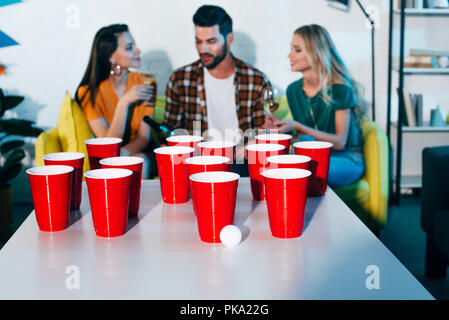 Vue rapprochée de gobelets en plastique et la balle pour la bière pong et jeune ami boire du vin derrière Banque D'Images