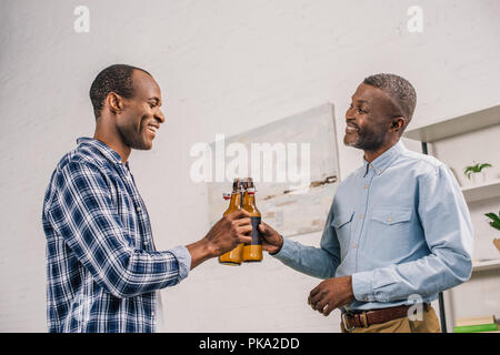 Happy père et fils adultes cliquetis de bouteilles de bière et autres à la maison chaque sourire Banque D'Images