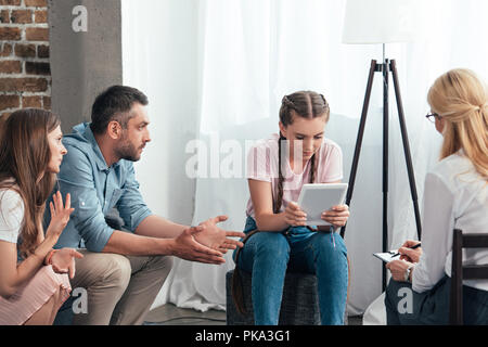 Les parents faisant des gestes de la main et d'essayer de parler avec teenage girl using digital tablet on séance de thérapie par conseillère in office Banque D'Images