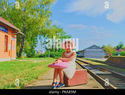 Adorable petite fille sur une gare, attendant le train avec vintage suitcase. Les voyages, vacances et enfance concept. Billet d'avion conc Banque D'Images