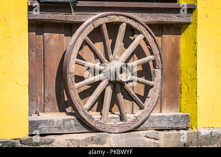 Roue en bois à partir d'un wagon des prairies debout contre un mur jaune Banque D'Images