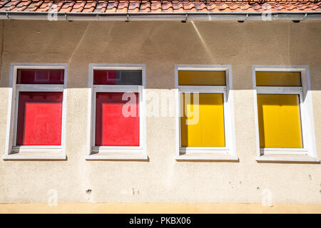 Quatre fenêtres colorées sur un bâtiment avec des rideaux rouge et jaune Banque D'Images