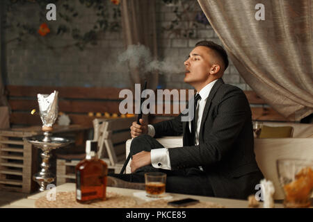 Beau jeune homme dans une robe cher fume un narguilé Banque D'Images