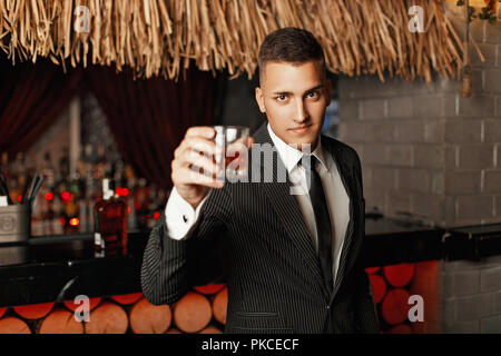 Beau jeune homme dans un costume élégant de boire du whisky au bar. Banque D'Images
