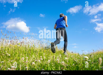 Low angle view of mature trail runner running uphill par wildflower meadow. UK Banque D'Images