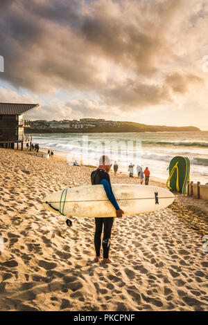 À la recherche d'un surfer sur la plage de Fistral Newquay en Cornouailles lors d'un coucher de soleil intense. Banque D'Images