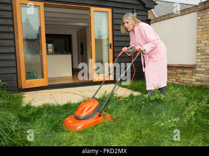 Woman mowing lawn portant une robe de chambre à l'extérieur Banque D'Images