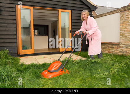 Woman mowing lawn portant une robe de chambre à l'extérieur Banque D'Images