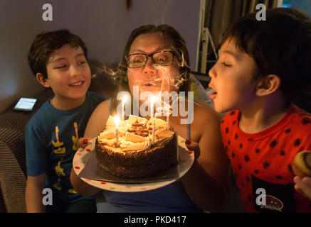 Une dame est aidé par sa famille, en soufflant les bougies sur son gâteau d'anniversaire au chocolat. Banque D'Images