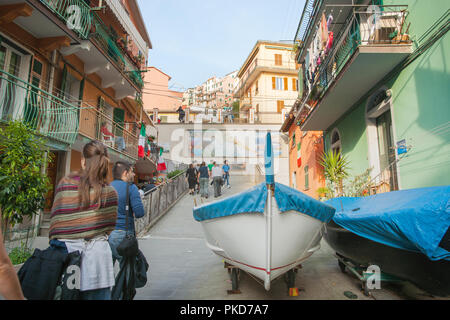 CINQUE TERRE, ITALIE - 25 avril 2011 ; bateaux tiré vers le haut dans une étroite rue du village en tant que touristes traversent à la recherche à l'architecture typique, boutiques et voile Banque D'Images