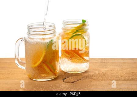 Les bocaux Mason en verre de limonade maison coulée avec tranches de citron, orange, citron vert, branche de menthe et de bulles sur fond de bois isolé Banque D'Images