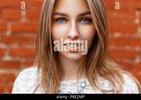 Beau portrait en gros plan d'une jolie femme aux yeux bleus sur un fond rouge. Banque D'Images