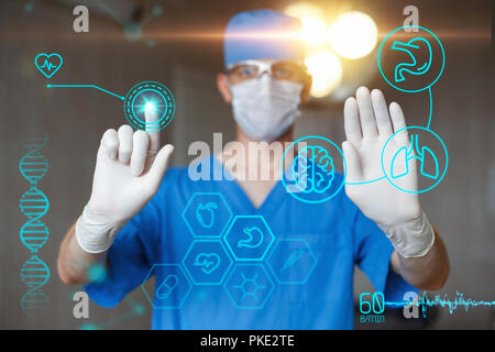 Médecin en uniforme bleu avec écran tactile l'infographie. Chirurgien professionnel moderne dans la salle d'opération. Les icônes sur le bureau. Banque D'Images
