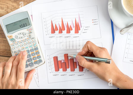 Businesswoman analyse graphiques statistiques a l'aide d'une calculatrice, vue de dessus de ses mains et les documents sur un bureau en bois. Banque D'Images