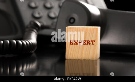 Cube de bois avec un expert signe sur elle à côté d'un téléphone fixe. De conceptuel et de support client professionnel précis et consulting. Banque D'Images