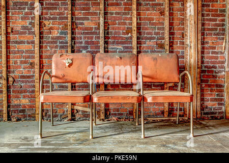 Trois anciens, couverts en plastique vinyle orange, l'armature en aluminium chaises dans un bâtiment abandonné. Banque D'Images