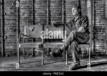 Portrait d'un fatigué middle-aged man assis sur une rangée de vieilles chaises. Banque D'Images